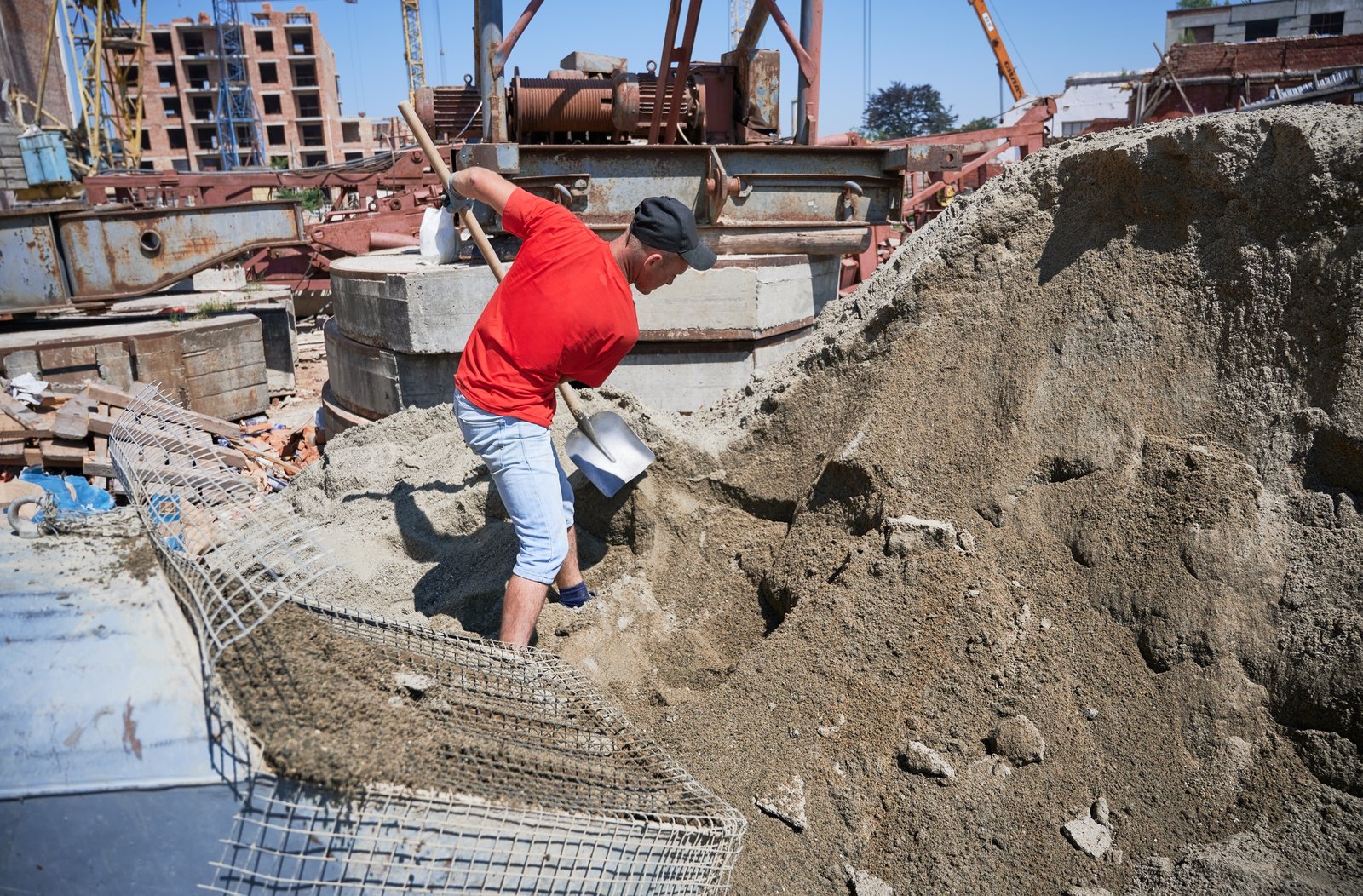 Male worker shoveling sand-cement mix at construction site.